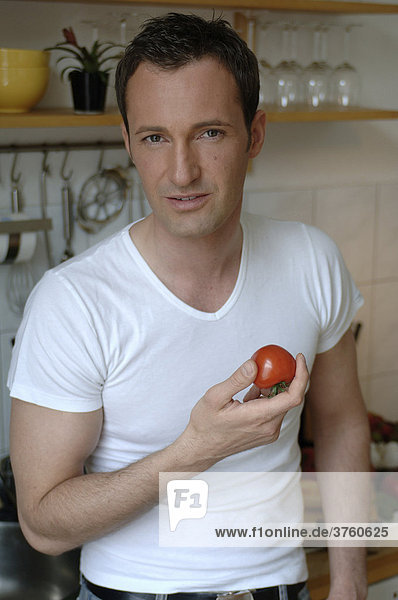 31-jähriger Mann isst Tomate in Küche