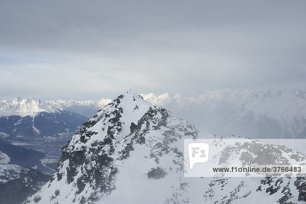Verschneiter Berggipfel mit Gipfelkreuz und Bergsteiger über dem Inntal bei starkem Föhnsturm  Tuxer voralpen Tirol Österreich