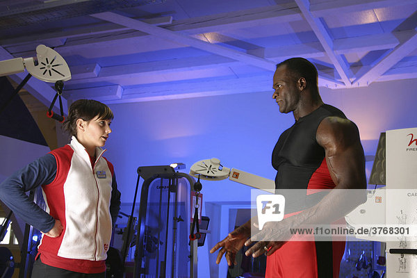 Fitnesstrainer übt mit einer jungen Frau an einer Seilzugmaschine in einem Sportstudio