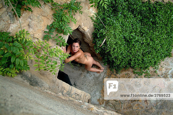 Perspektivische Ansicht einer nackten  jungen Frau stehend im Torbogen eines Natursteingarten  Mallorca  Spanien