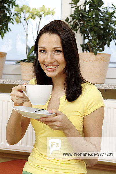 Young woman smiles over a cup of coffee