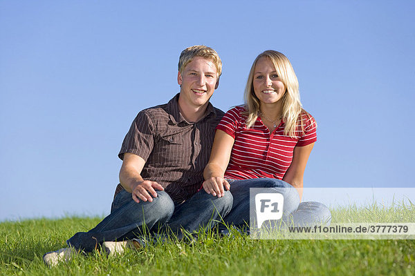Ein junges Paar  er 22  sie 20  sitzt nebeneinander auf einer Wiese