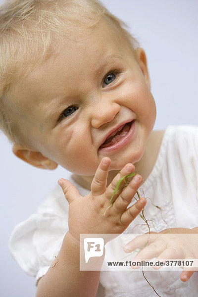 Ein 10 Monate altes Mädchen spielt mit Grashalmen