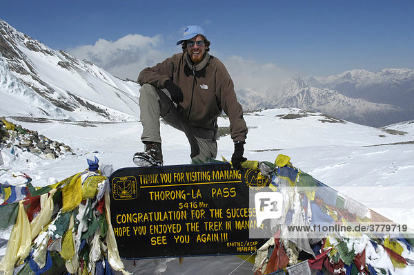 Successful mountaineer at the sign with prayer flags in the snow Thorung La Pass 5416 m Annapurna Region Nepal