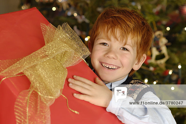Kind freut sich über eine Geschenk an Weihnachten unter dem Christbaum