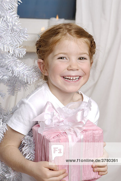 Kind freut sich über eine Geschenk an Weihnachten unter dem Christbaum