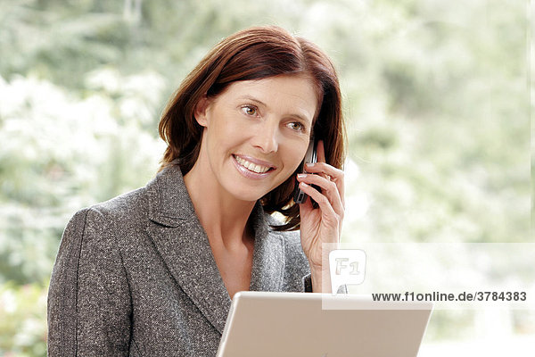 Geschäftsfrau telefoniert lachend  mit Laptop
