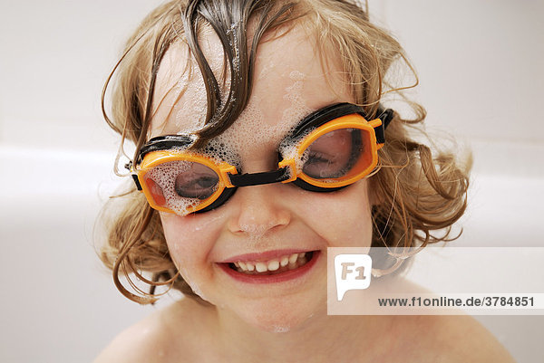 Little girl wearing goggles sitting in a bath tub