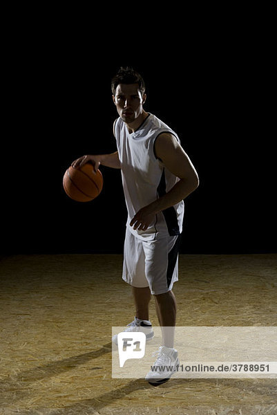 Ein Basketballspieler dribbelt einen Ball  Porträt  Studioaufnahme