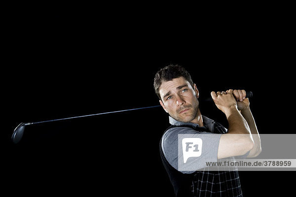 Ein Golfer schwingt einen Schläger  Porträt  Studioaufnahme