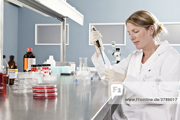 Ein Labortechniker  der eine Probe mit einer Pipette in ein Fläschchen gibt.