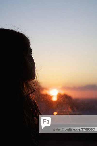 A girl looking out a window at sunset