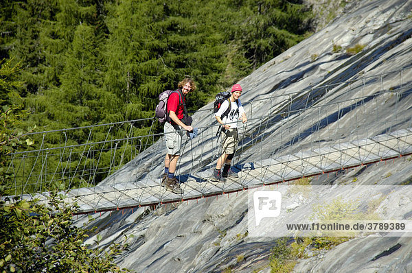 Paar Wanderer geht über eine Hängebrücke unterhalb des Glacier de Bionnassay Hochsavoyen Haute-Savoie Frankreich