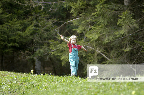 Ein dreijähriges Mädchen läuft Wiese hinunter im Frühling