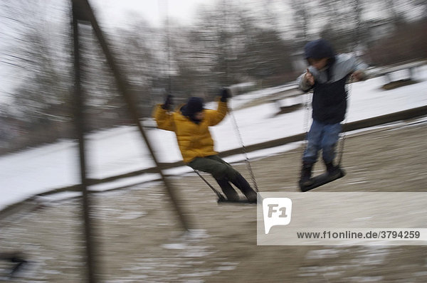 Two boys on swings at a playground in winter