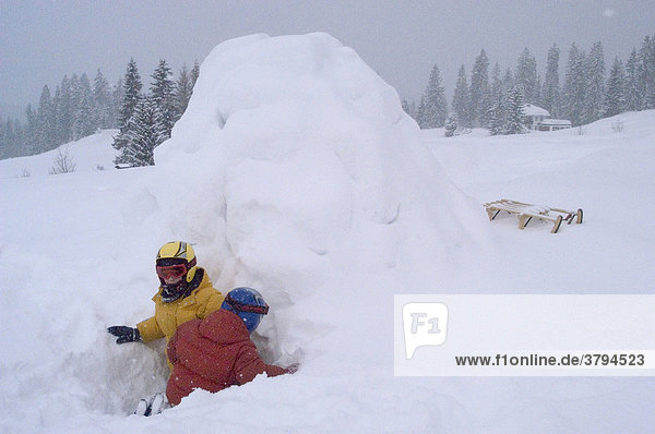 Zwei Kinder spielen vor selbst gebautem Iglu im Schnee