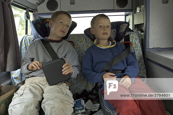 Zwei müde sechs und acht Jahre alte Jungen auf dem Rücksitzt eines VW Campingbusses