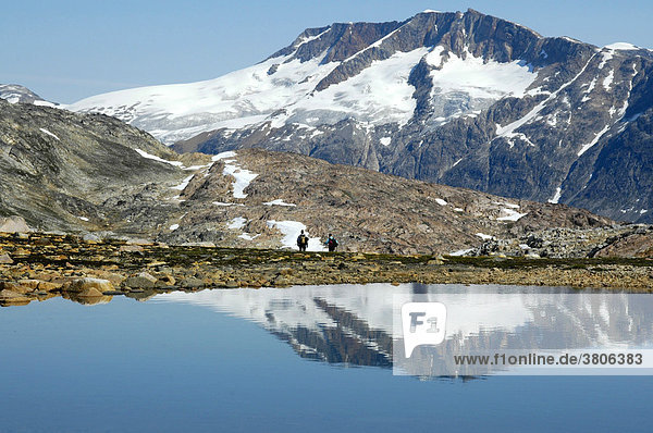 Zwei einsame Wanderer vor Berg mit Gletscher Spiegelung im See bei Tiniteqilaaq Ostgrönland