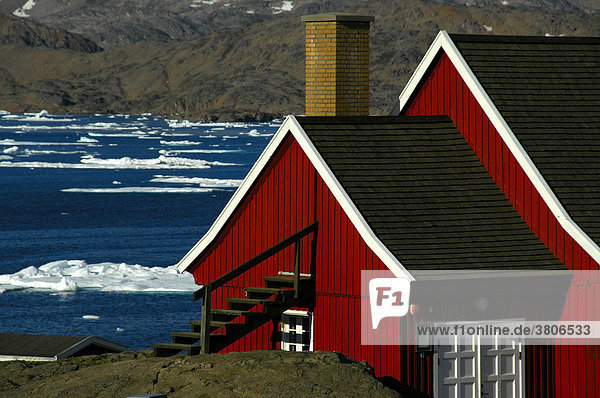 Rotes Haus überm Fjord mit Packeis Ammassalik Ostgrönland