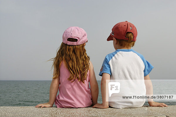 Kinder sitzen auf einer Mauer am Meer