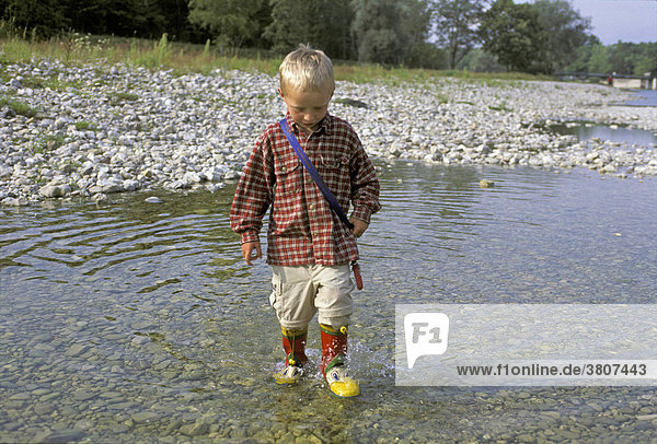 Kleiner Junge  4 Jahre  läuft mit Gummistiefeln durchs Wasser  Isar bei München  Deutschland