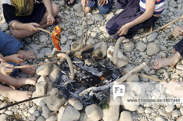 Kinder beim Würstel grillen am Feuer