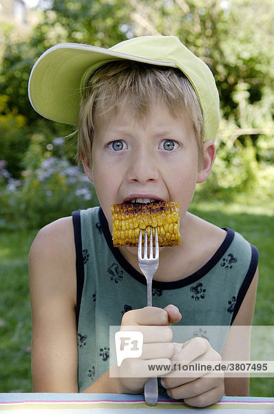 Junge  elf Jahre  ißt gebratenen oder gegrillten Maiskolben