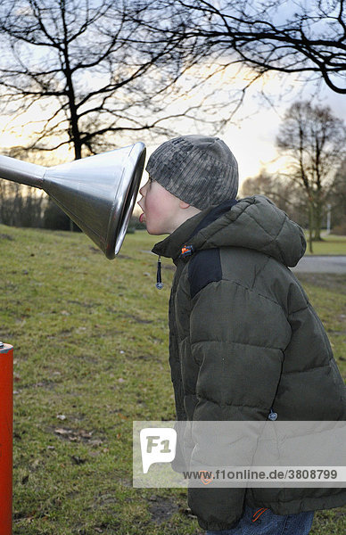 Little boy sticking his head into the funnel of an intercom in a playground