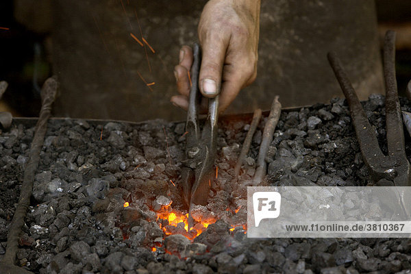 Schmied mit traditionellen Werkzeugen hält Eisen in die Glut