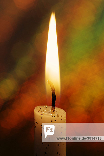 Burning candle in front of a colourful background