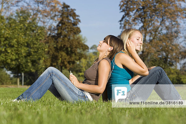 Zwei Freundinnen sitzen in einem Park und hören gemeinsam Musik