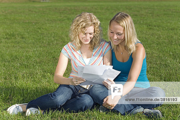Zwei Freundinnen sitzen in einem Park und lesen gemeinsam einen Brief