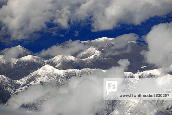 Blick von oben auf schneebedeckte Gebirgszüge umgeben von Wolken Tibet China