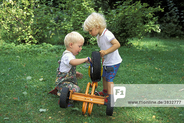 Two three year old boys repairng tricycle MR