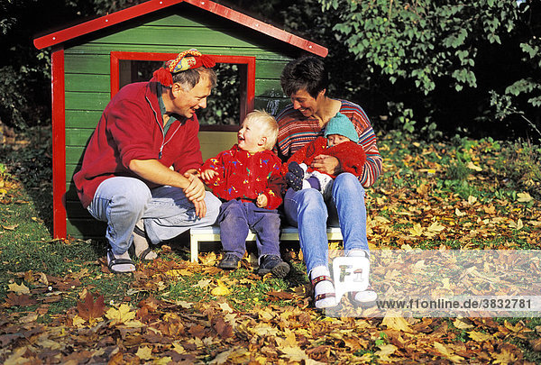 Mother - father - and two-year-old boy in front of a toy house in autumn MR