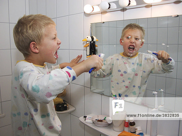 Little seven-year-oldboy in pyjamas brushing his teeth reflecting in mirror