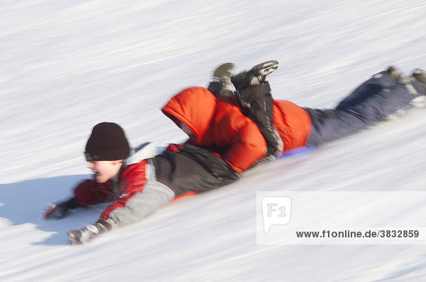 Two children sliding on their bellies downhill