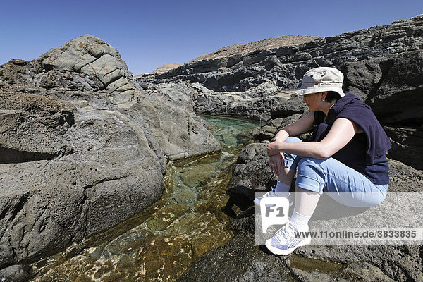 Frau sitzt an einem Gezeitentümpel - Felsküste in Aguas Verdes - Playa del Valle   Fuerteventura   Kanarische Inseln