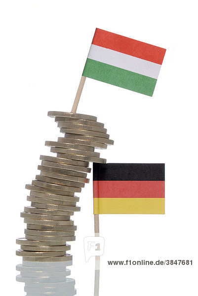 Wackliger Stapel Euromünzen der von einer Deutschlandfahne gestützt wird  darauf eine Ungarnfahne  Symbolbild für Finanzkrise des Euro