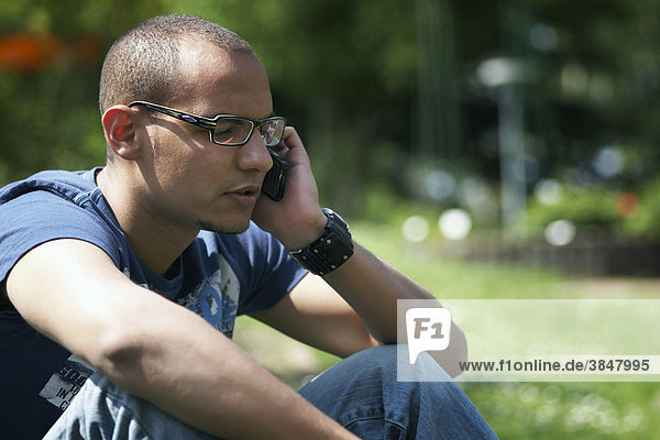 Junger Mann mit Handy telefonierend im Park