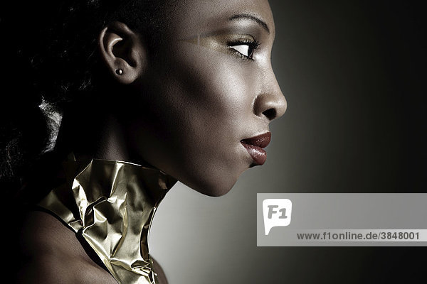 Seitliches Portrait einer jungen dunkelhäutigen Frau mit einem goldenen Halsband