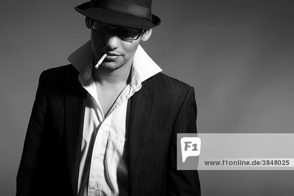 Young man in suit  shirt  tie and hat  with a cigarette in his mouth and looking cool