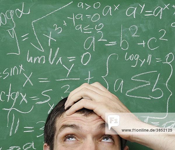 Verwirrter Mann vor mathematischen Formeln auf einer Kreidetafel