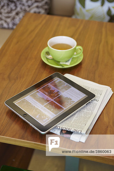 EBook Lesegerät iPad mit Teetasse und Tageszeitung auf Holztisch