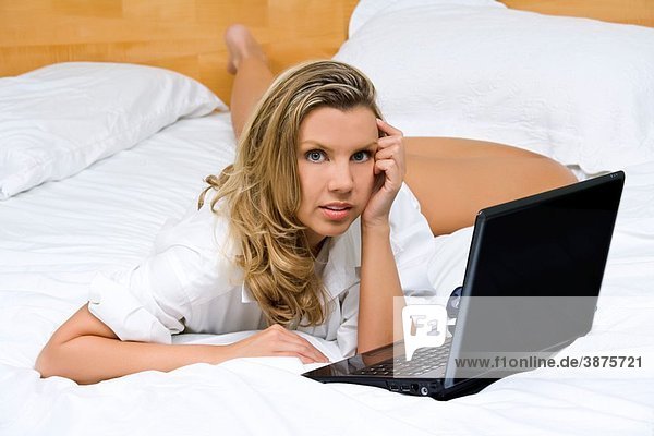 Beautiful caucasian woman laying in bed working on a laptop computer