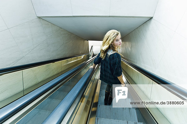 Teenagerin auf Rolltreppe  Blick über die Schulter zur Kamera