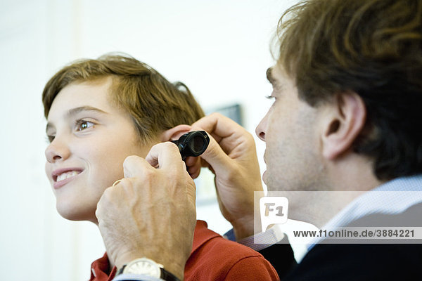 Doctor examining young patient's ear with otoscope