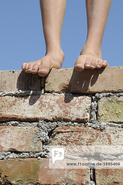 Füße eines Jungen auf einer Ziegelmauer