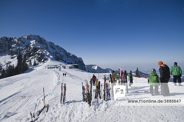 Rast in der Wintersonne  im Schnee aufgestellte Skier und Stöcke  daneben genießen Wintersportler die Aussicht auf das winterliche Priental  Aschau  Bergstation Kampenwandbahn  Chiemgau  Bayern  Deutschland  Europa