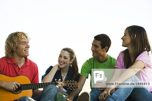 Junge Freunde hängen herum  einer spielt Akustikgitarre.